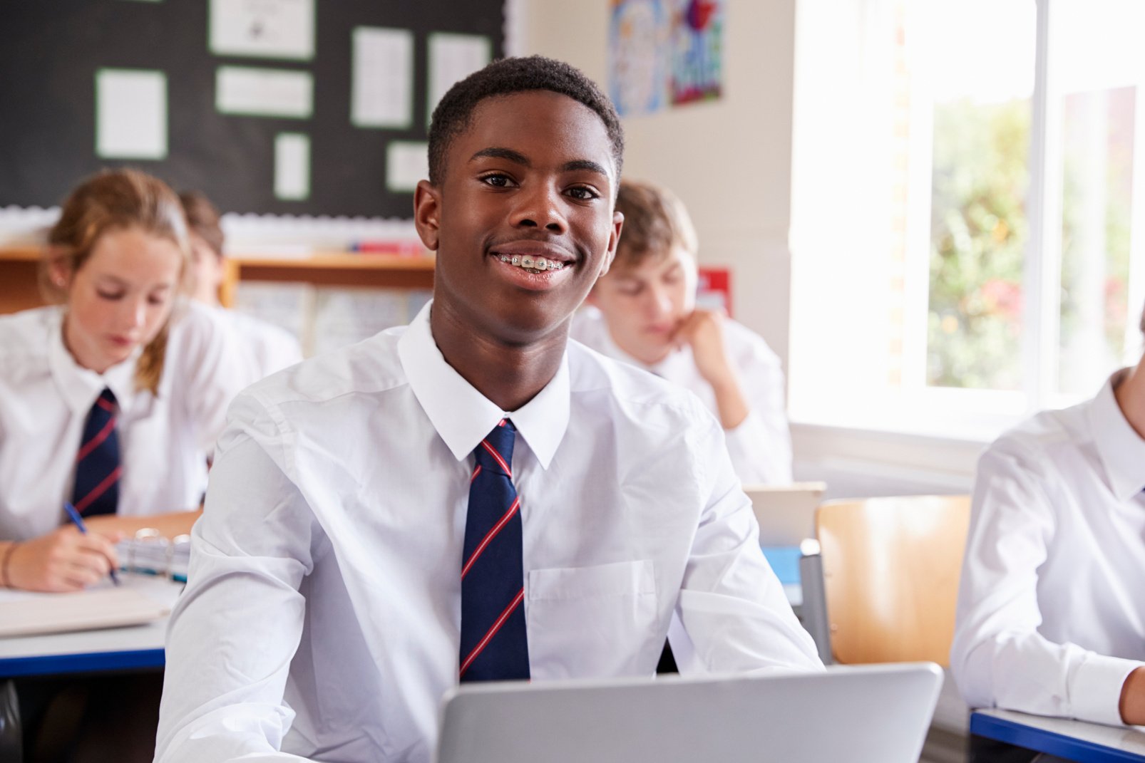 Male Pupil in Uniform Using Laptop in Classroom